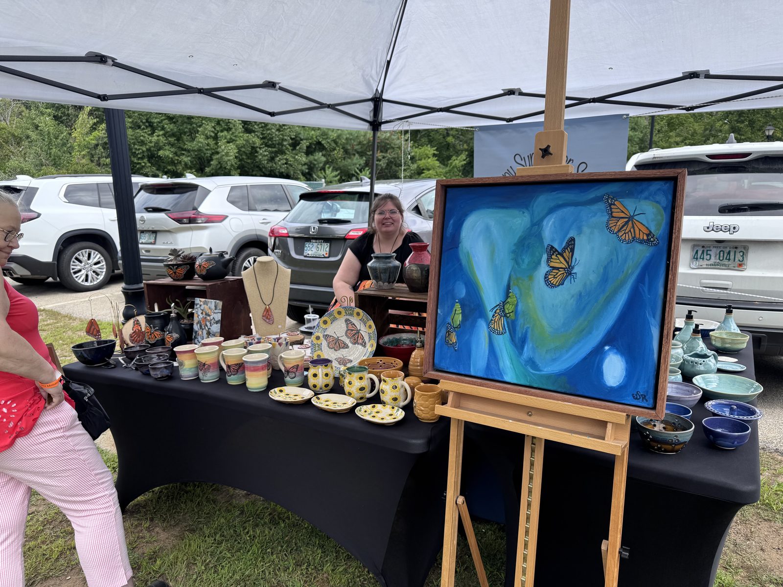 Artist showcasing monarch-themed paintings and handmade pottery