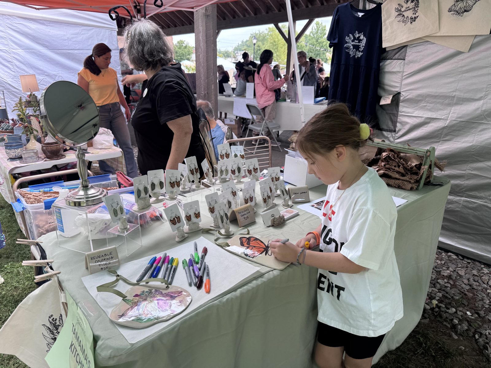 A vendor helping a young visitor at a craft table