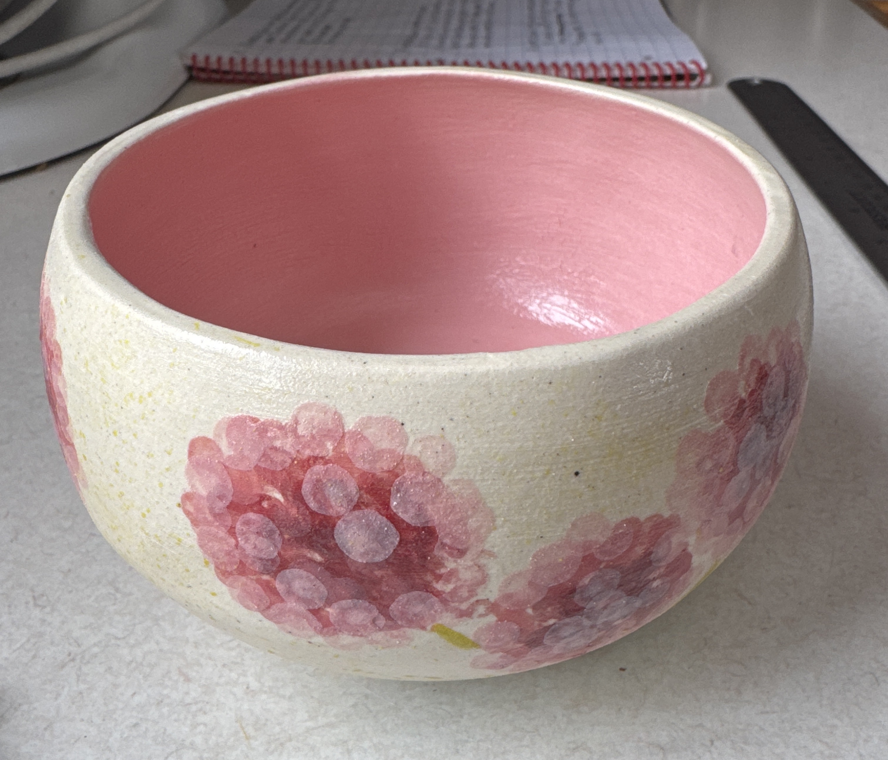 A handmade ceramic bowl with a pink glazed interior and painted floral pattern
